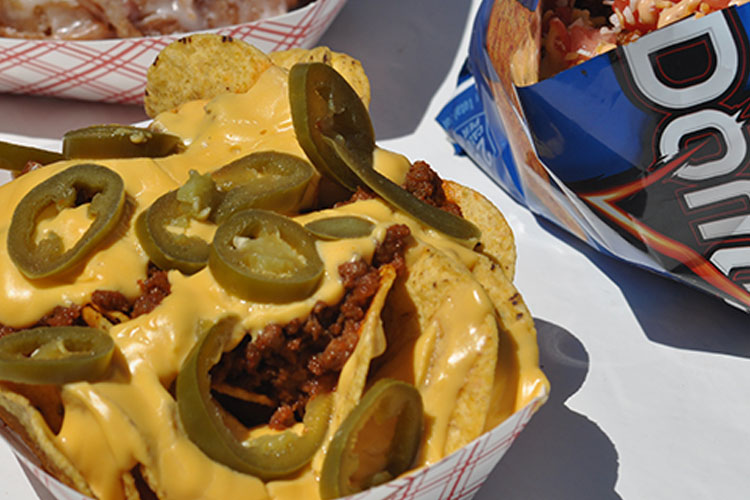 A close up image of nachos with meat and jalapenos on them with an open blue bag of Doritos to the right.